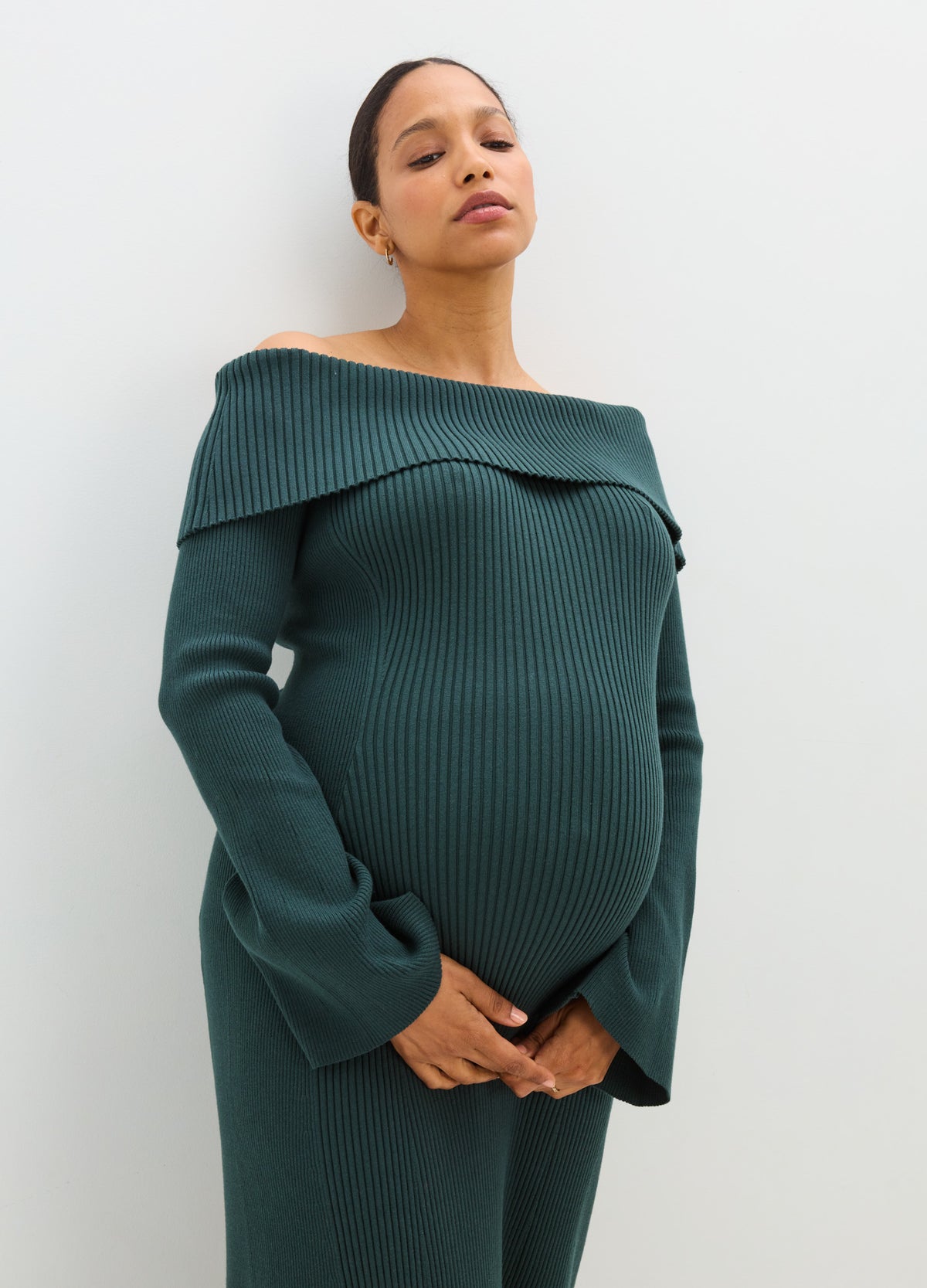 Pregnant model wearing a dark teal ribbed off-the-shoulder sweater dress with long sleeves and a fitted maternity silhouette.