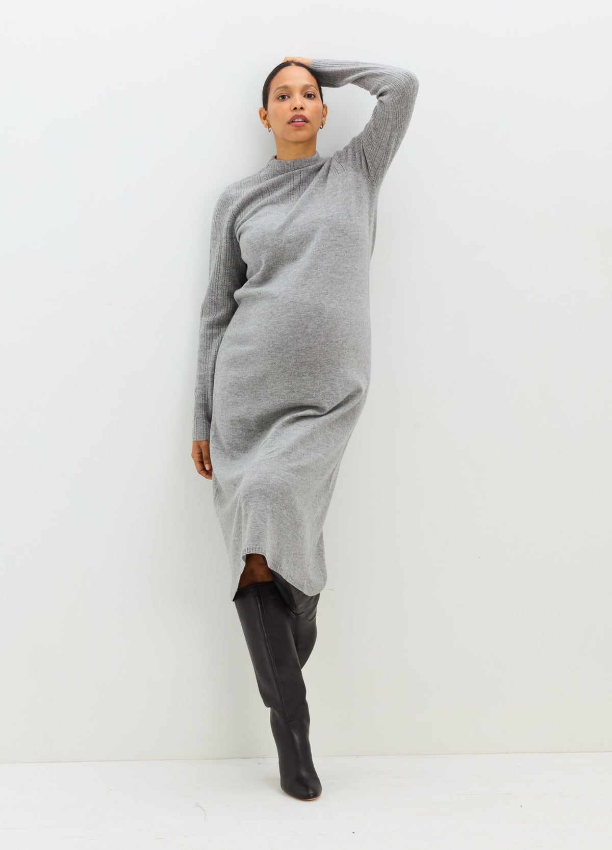 Pregnant model wearing a gray long-sleeve pointelle knit maternity dress with a fitted waist and midi hem.