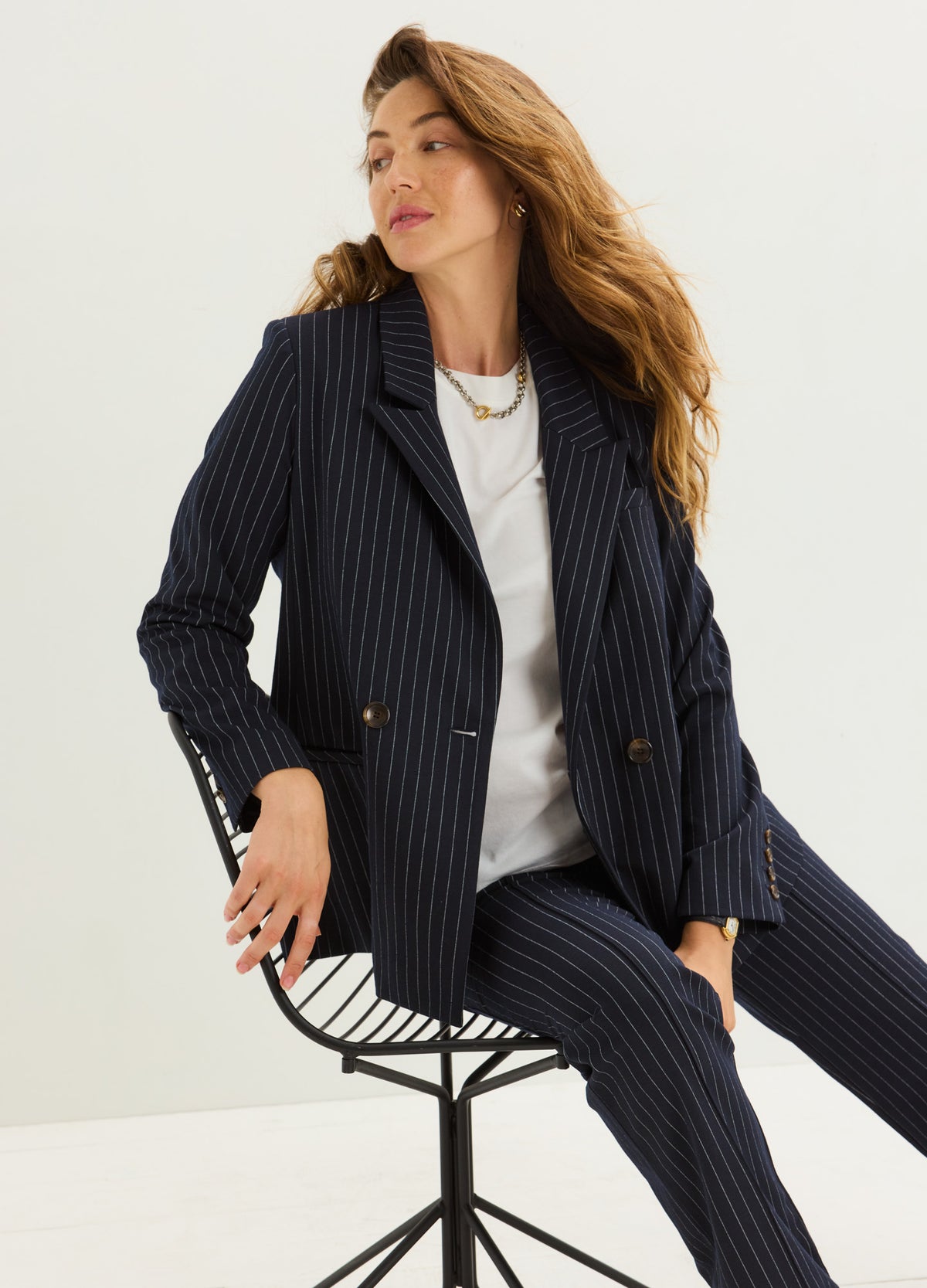 Pregnant model wearing a navy pinstripe maternity blazer with gold buttons over a white top.