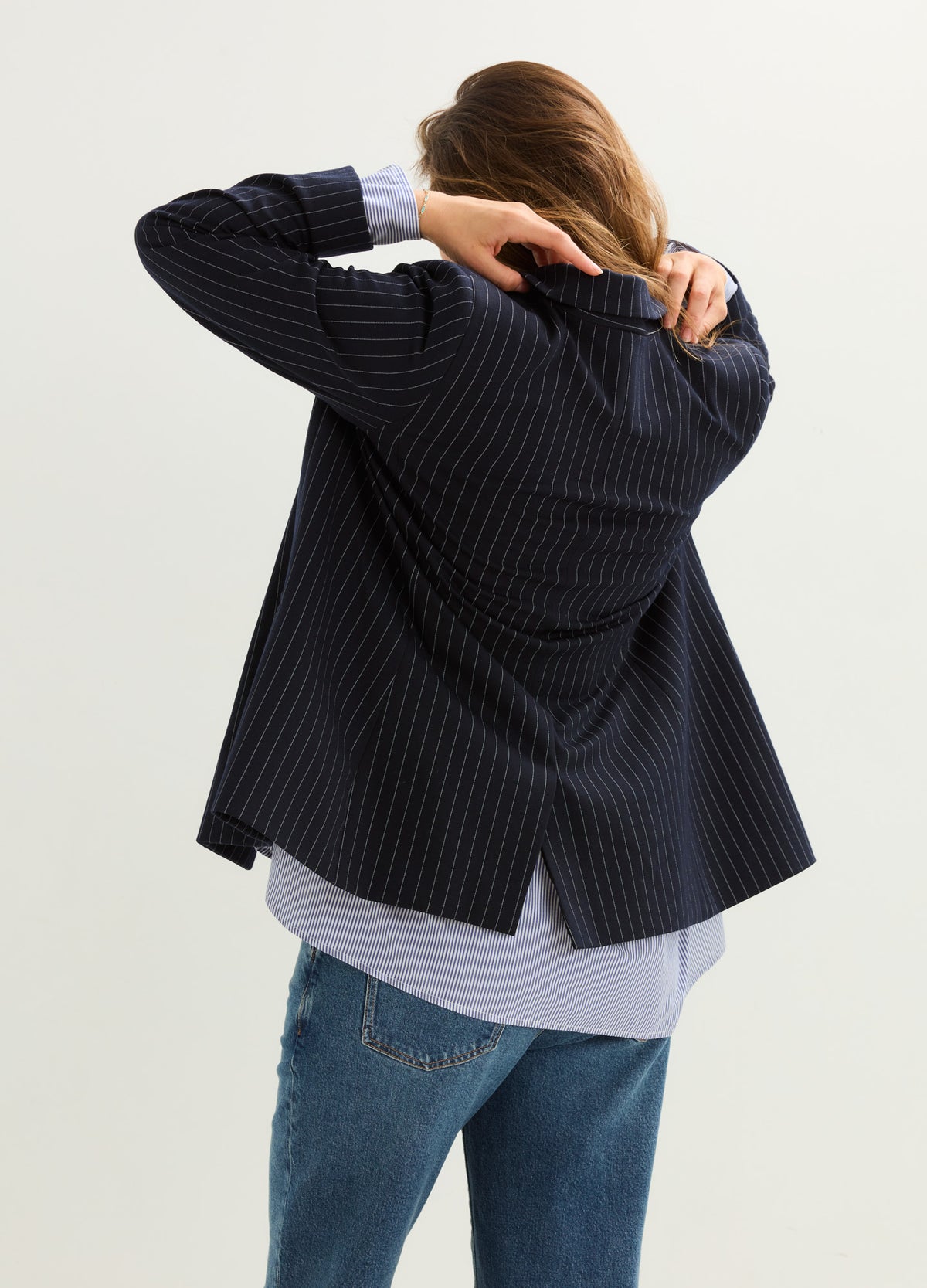 Pregnant model wearing a dark navy pinstripe maternity blazer with a relaxed fit and flared hem.