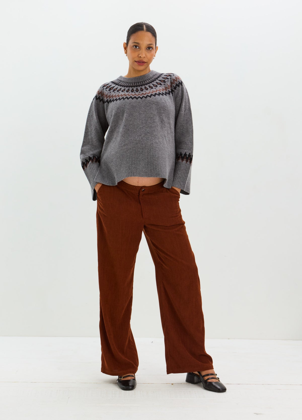 Gray knit sweater with voluminous sleeves and a colorful Fair Isle yoke, styled with rust-brown trousers.