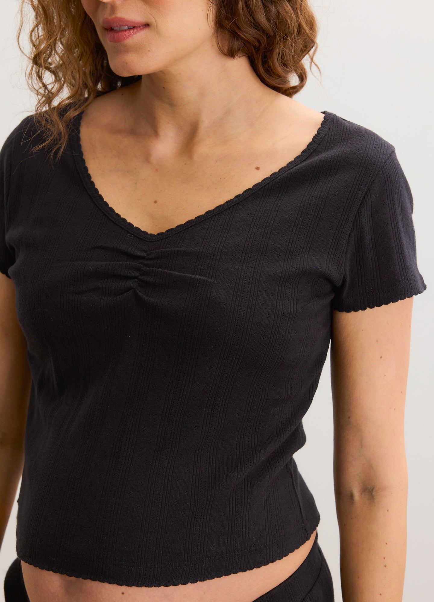 Black short-sleeve maternity tee with sweetheart neckline and delicate pointelle trim, fitted silhouette.