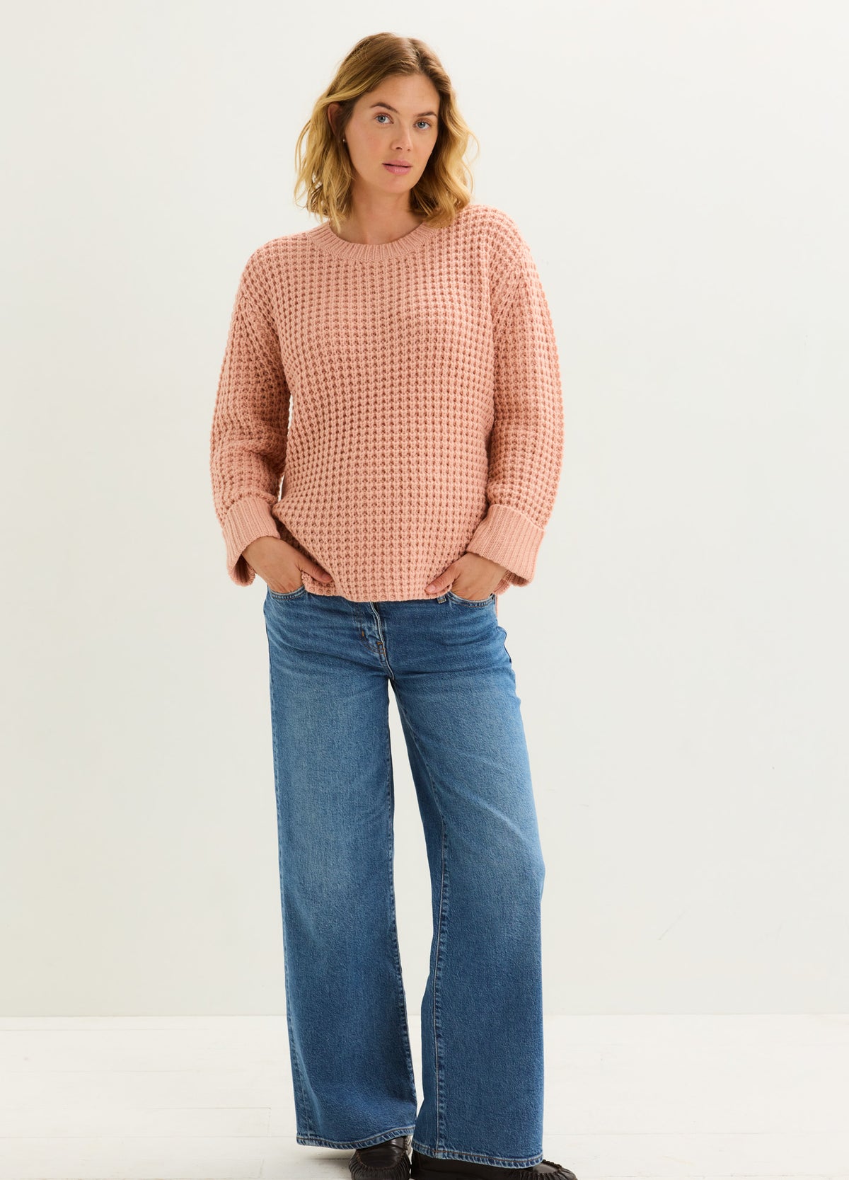Pregnant model wearing relaxed blue wide-leg maternity jeans with a soft peach sweater.