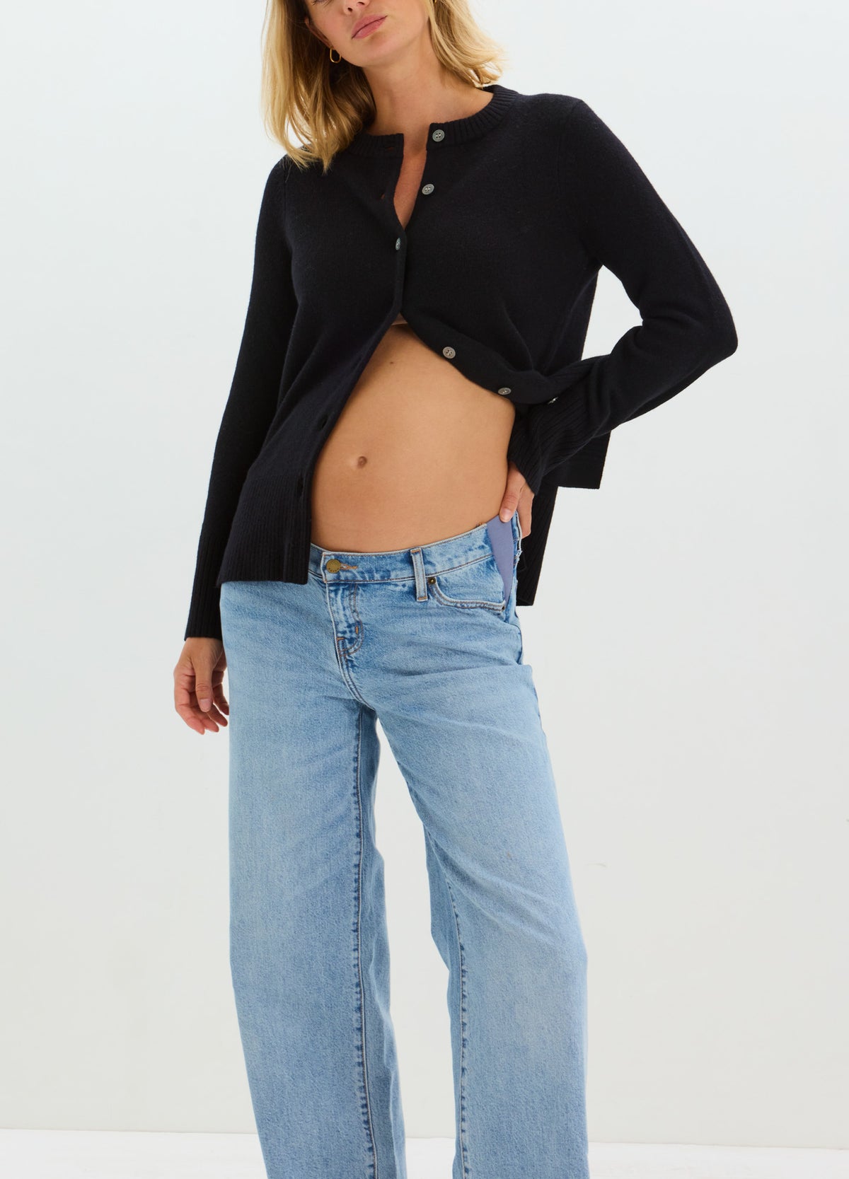 Pregnant model wearing light blue relaxed wide-leg maternity jeans with a supportive belly panel and black cardigan.