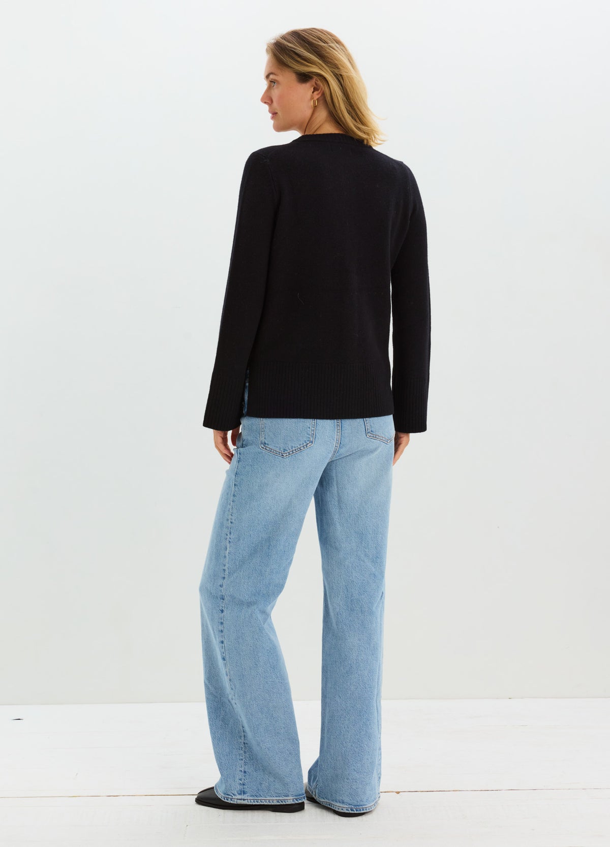 Pregnant model wearing relaxed light-blue wide-leg maternity jeans and a black long-sleeve top.