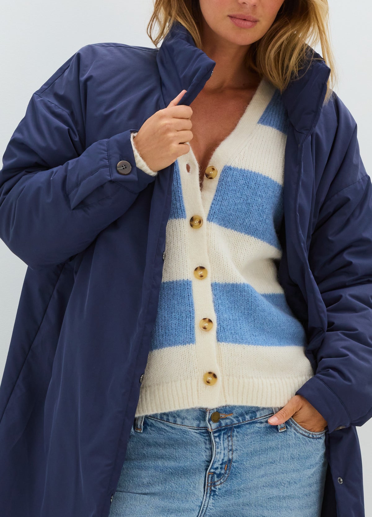 Navy quilted coat with a relaxed fit, worn open over a blue-and-cream striped cardigan.