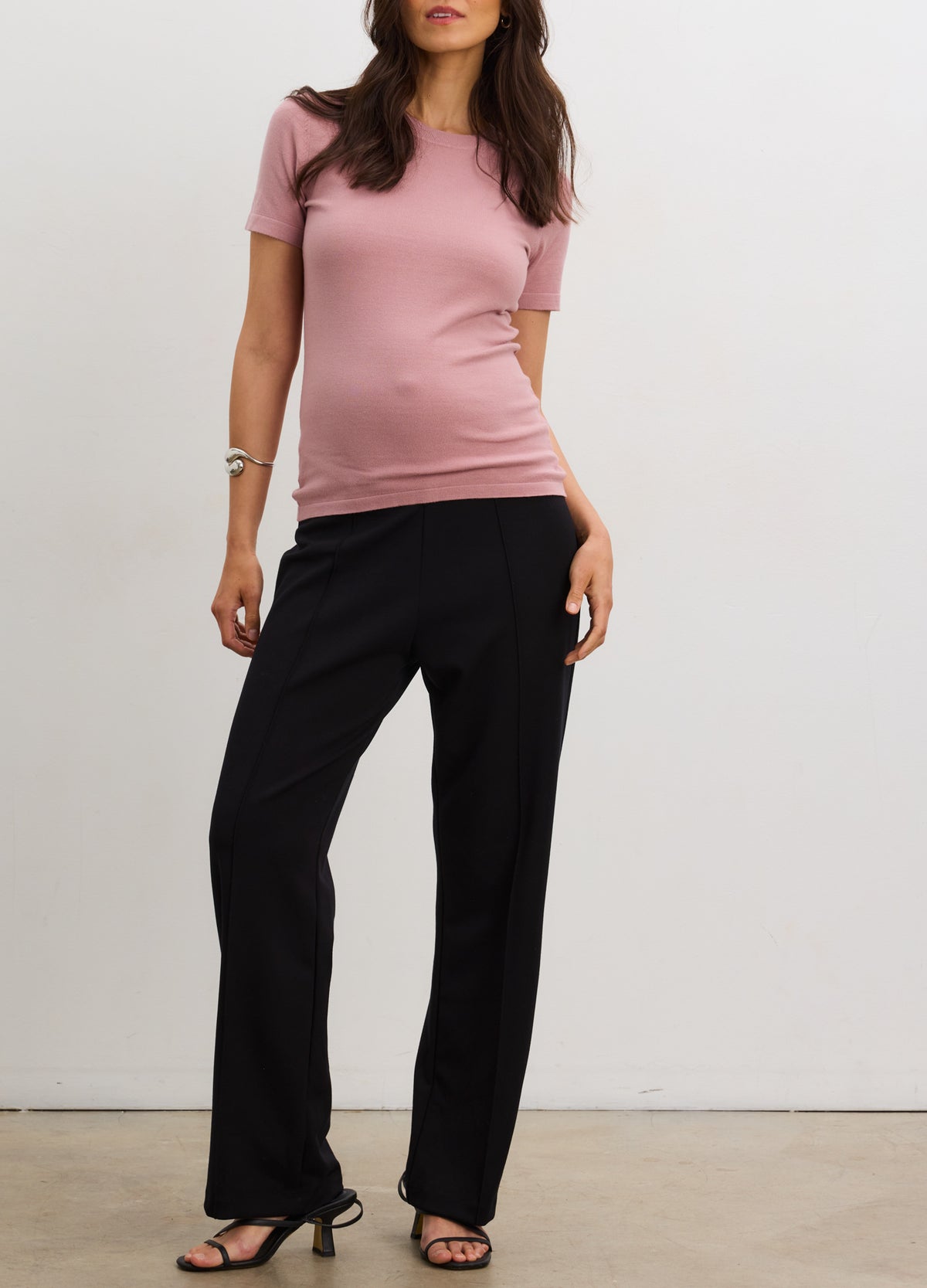 Black maternity stretch straight-leg work pants with seamed detail worn with pink short-sleeve top and black heels.