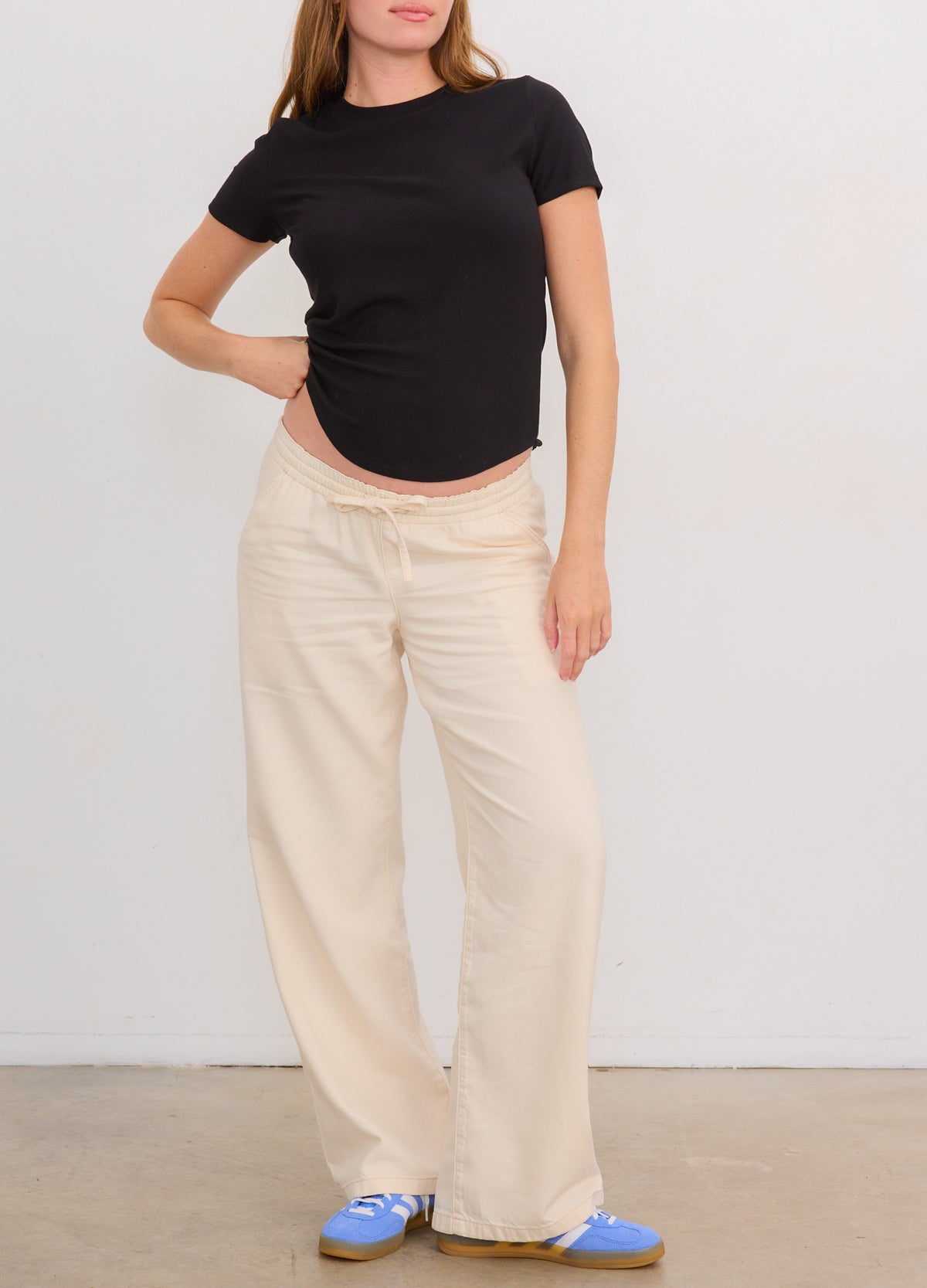 Black short-sleeve ribbed maternity tee paired with loose beige wide-leg pants and blue slip-on shoes.