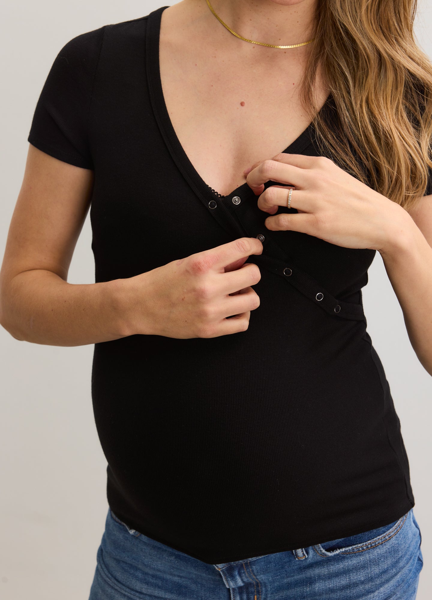 Black short-sleeve maternity tee with soft knit fabric and front snap closure, fitted over pregnant belly.