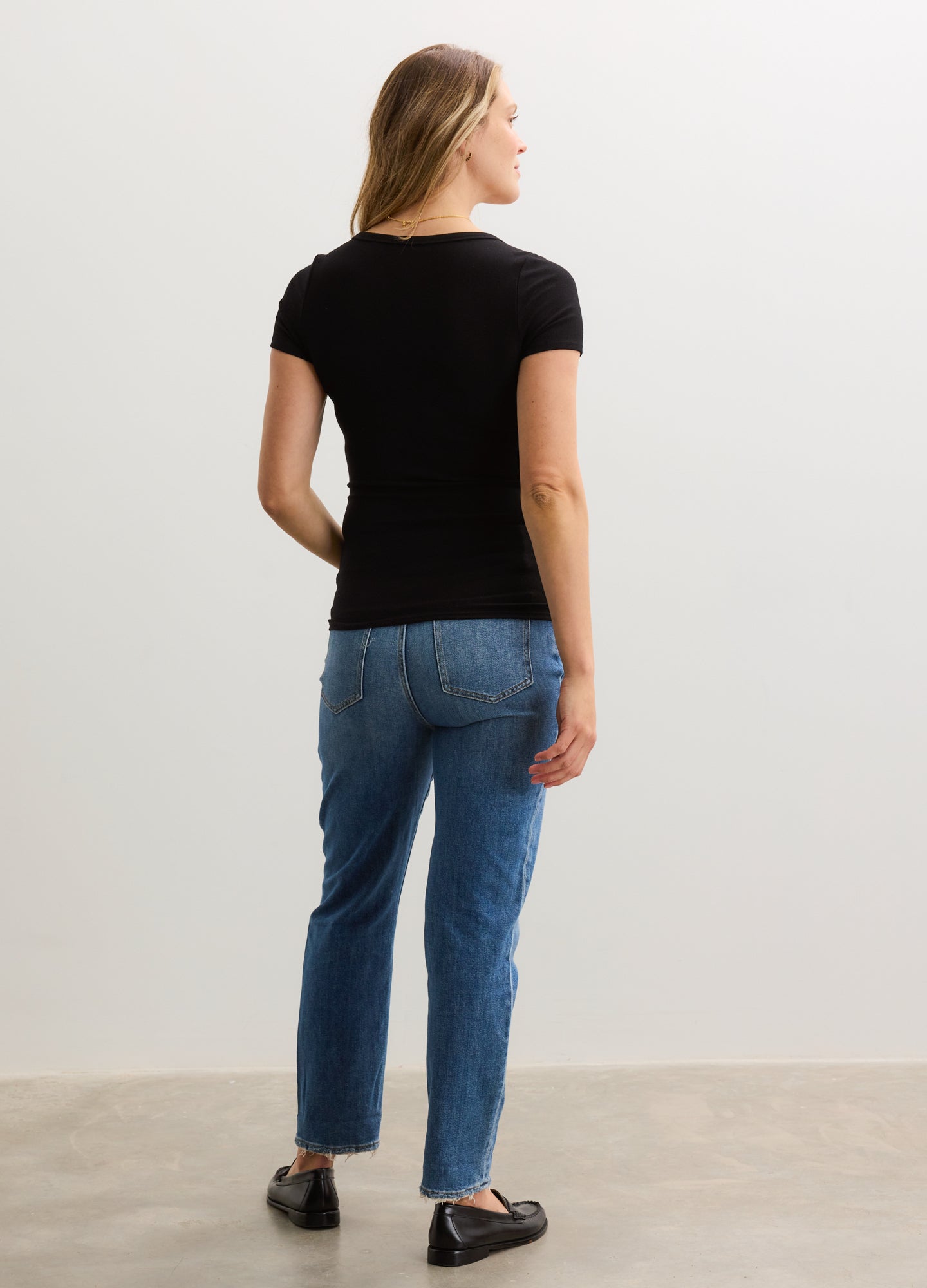 Black short-sleeve knit tee with fitted silhouette, worn by pregnant model, paired with relaxed blue jeans and black shoes.