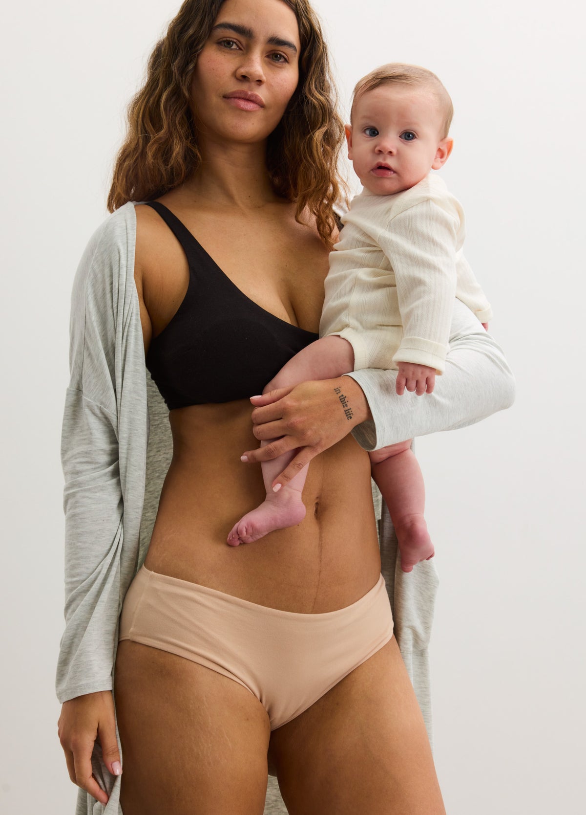 Light gray softluxe maternity robe open over black nursing bra and beige seamless underwear on pregnant woman holding baby.