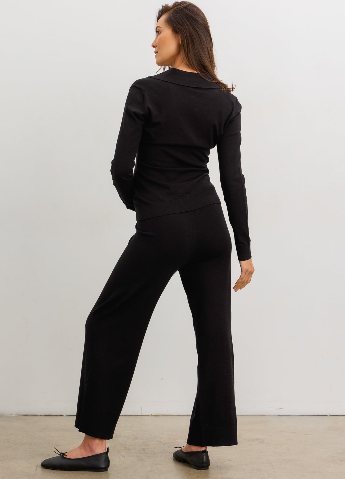 Black knit maternity nursing polo with long sleeves and relaxed straight-leg pants modeled from the back.