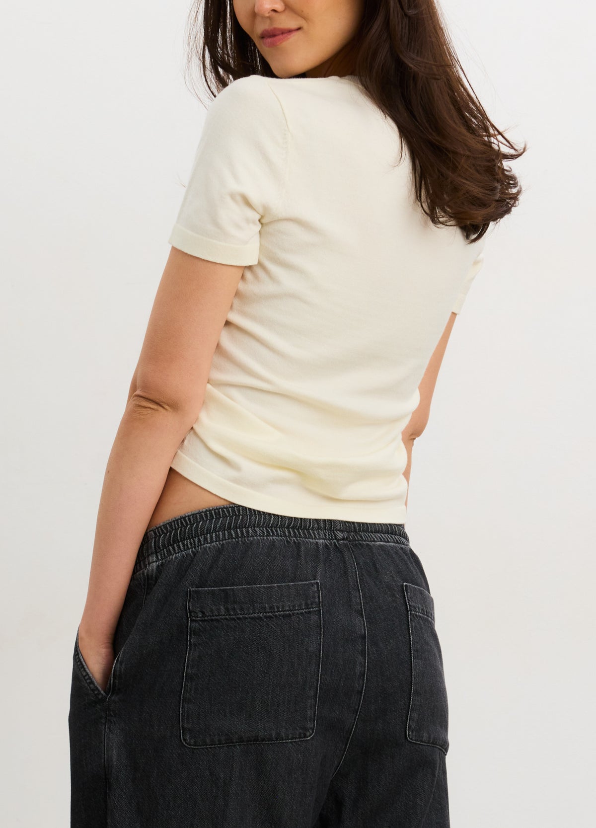 Cream-colored fitted knit tee with short sleeves, designed to contour a pregnant belly, paired with dark denim jeans.