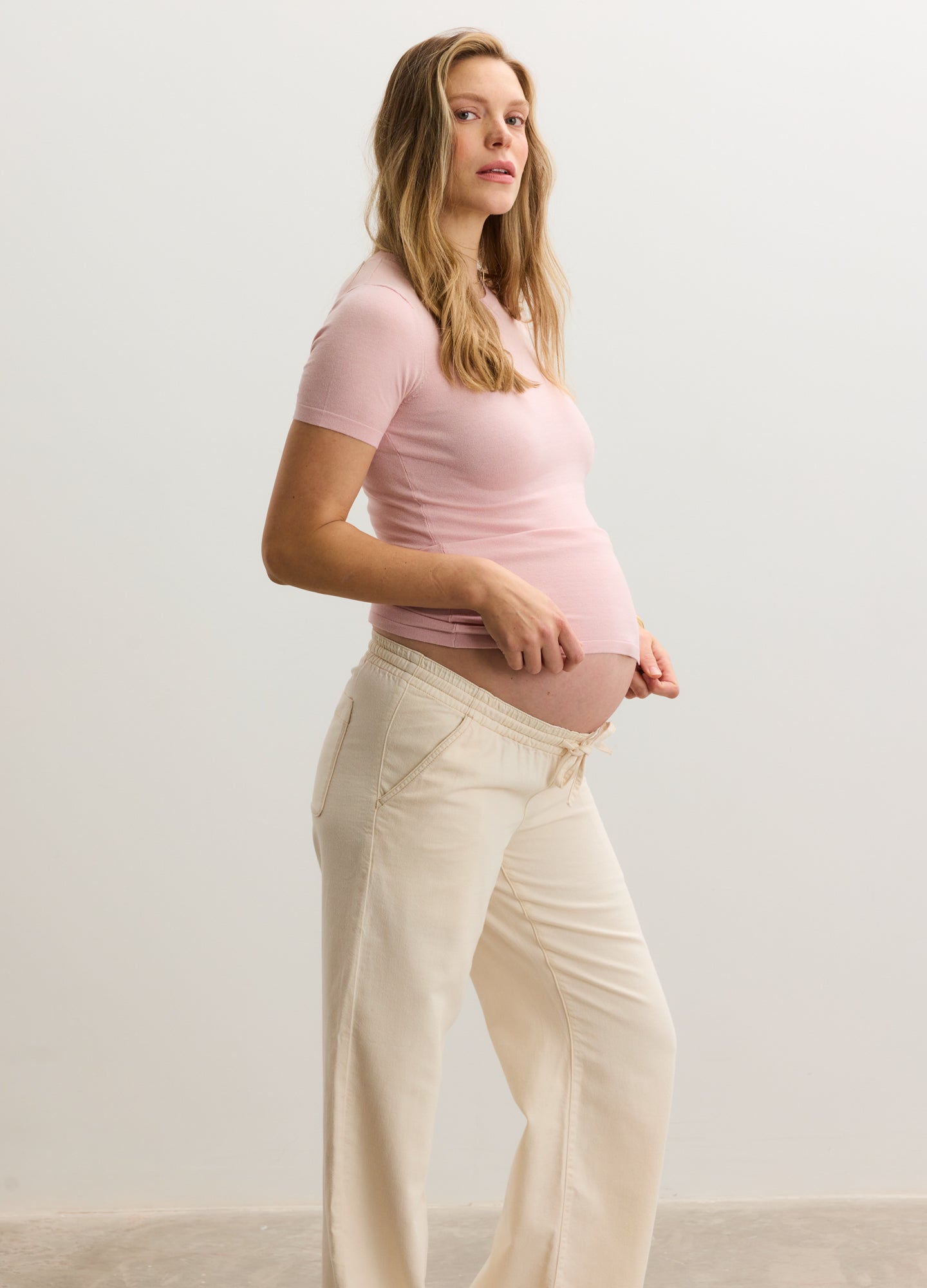 Light pink short-sleeve knit maternity tee paired with cream-colored maternity pants.