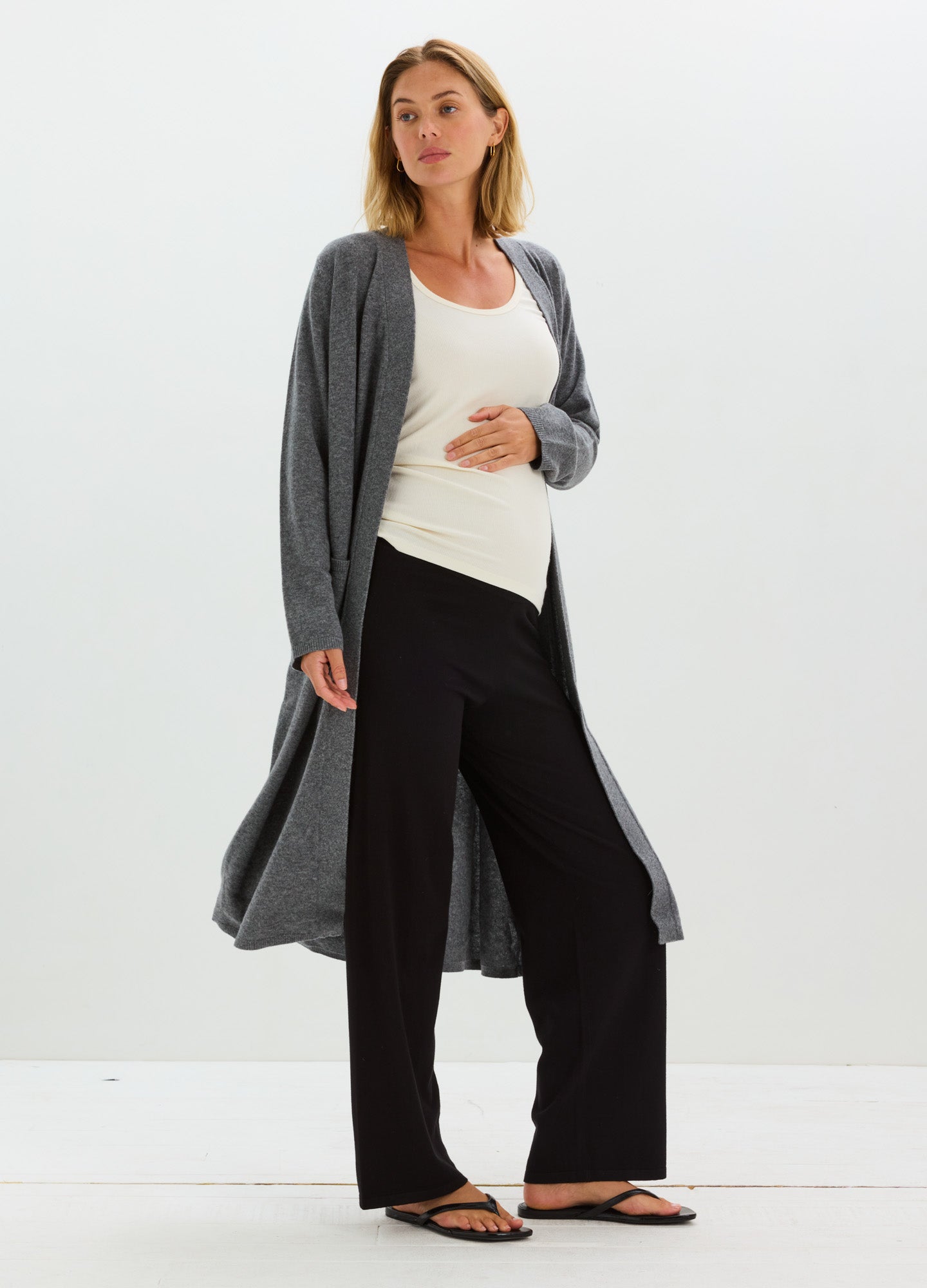 Maternity black wide-leg knit pants with a high stretchy waistband paired with a cream tank top and long gray cardigan.
