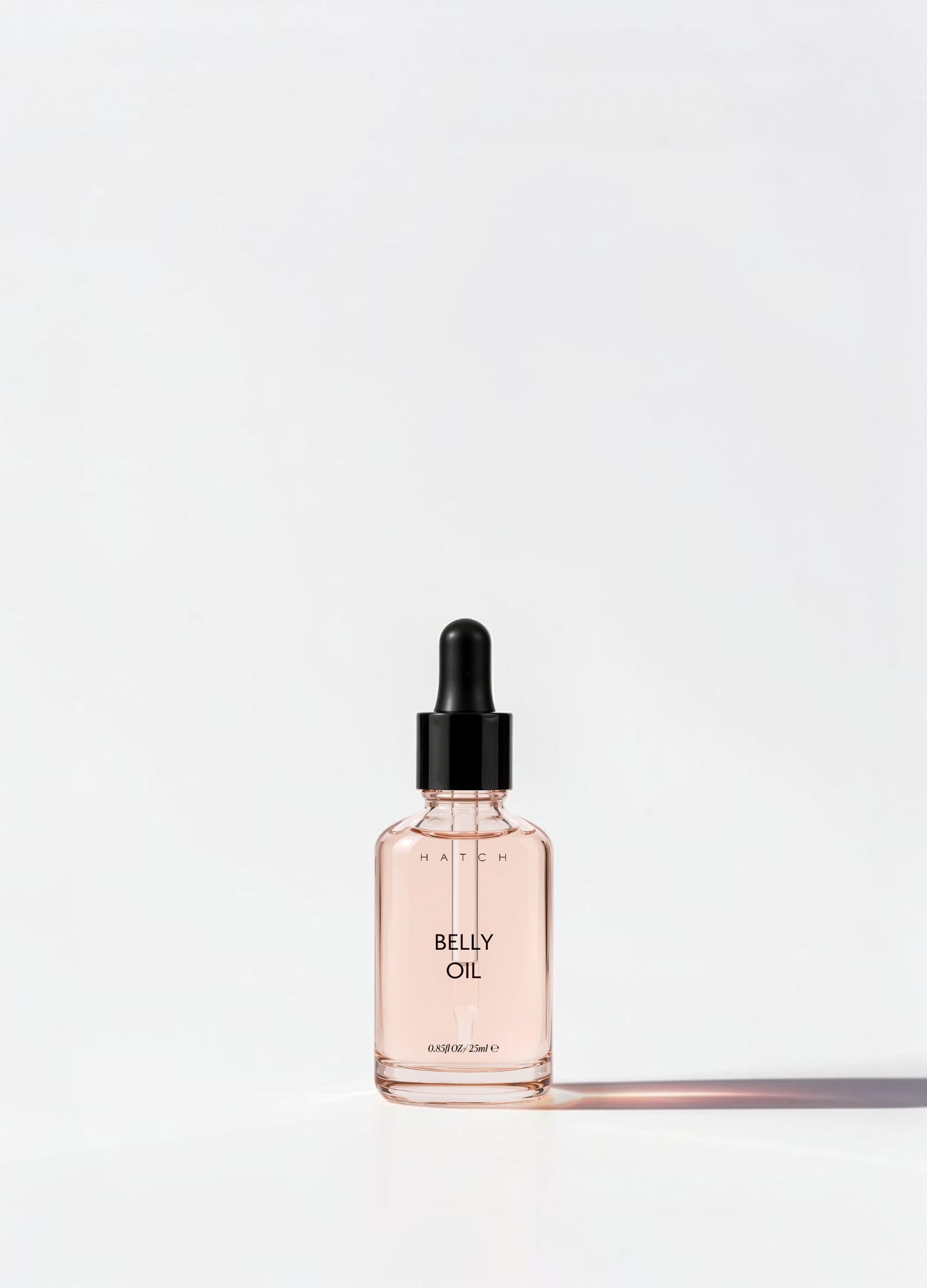 Small rectangular glass bottle of light pink belly oil with black dropper cap for maternity care.