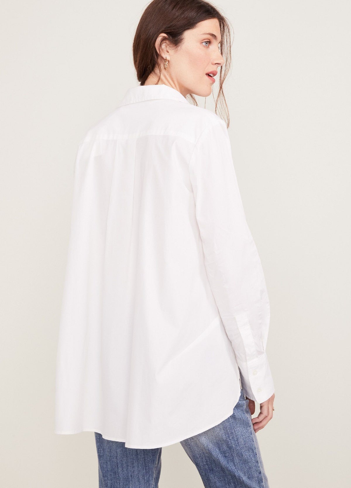 The Classic Buttondown - White maternity buttondown shirt with long sleeves and nursing-friendly front buttons, worn loose over black pants.